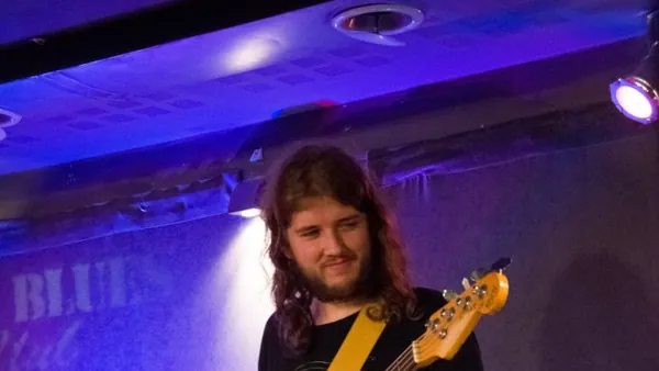 Mateusz Pawelec z gitarą basową w niebieskim świetle, za nim perkusista
