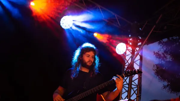 Mateusz Pawelec gra na gitarze basowej w świetle kolorowych reflektorów