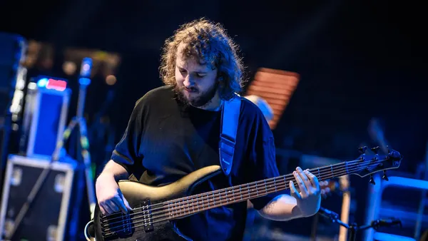 Mateusz Pawelec gra na pięciostrunowej gitarze basowej w niebieskim świetle