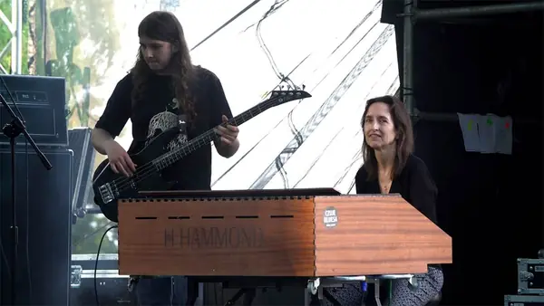 Mateusz Pawelec z gitarą basową na plenerowej scenie, obok klawiszowczyni przy organach