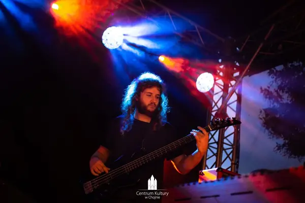 Mateusz Pawelec gra na gitarze basowej w świetle kolorowych reflektorów