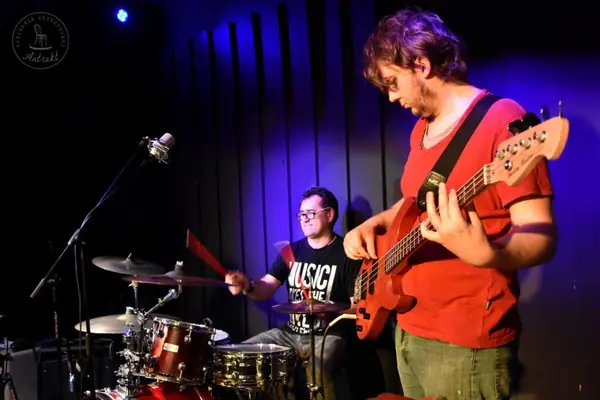 Basista z czerwoną gitarą basową i perkusista grają na scenie w fioletowym świetle